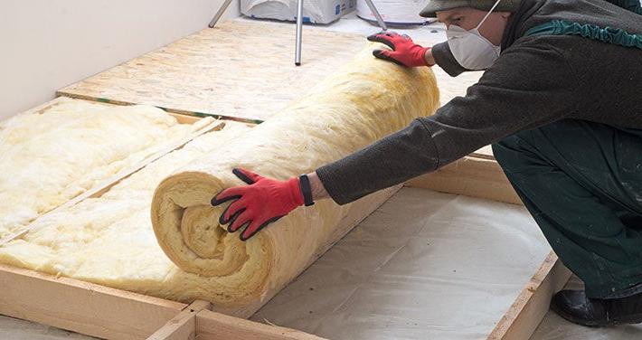 person wearing gloves while rolling out insulation